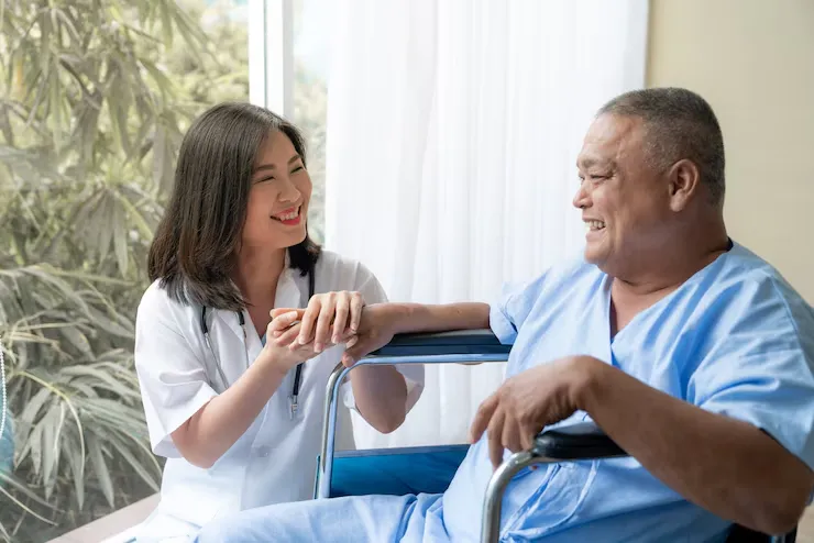 An Asian man in a wheelchair sits beside a nurse, who is engaged in conversation and offering care An Asian man in a wheelchair sits beside a nurse, who is engaged in conversation and offering care